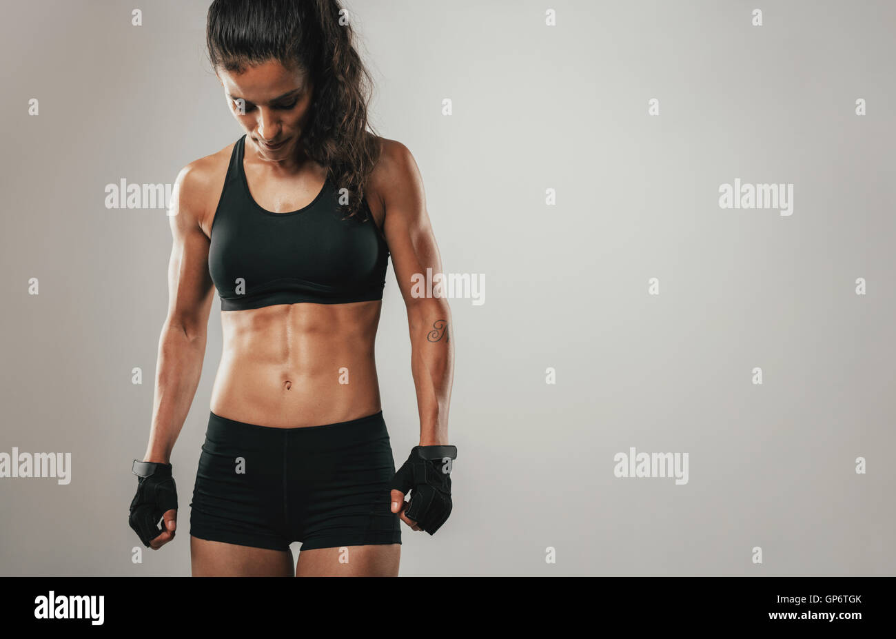 Fit healthy young female athlete with a toned strong body standing looking down, cropped three quarter view on grey with copy sp Stock Photo