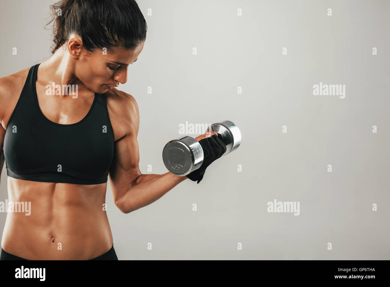 Cropped front view of woman in black shirt and weight training gloves lifting single chrome finish dumbbell with bicep muscles Stock Photo