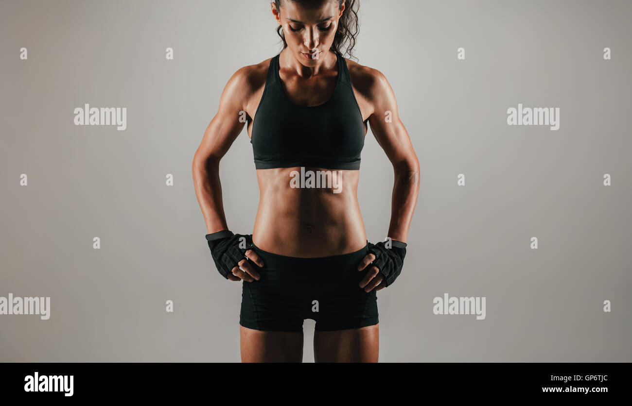 Trim abdominal muscles of woman with gloved hands on hips over gray background with copy space Stock Photo