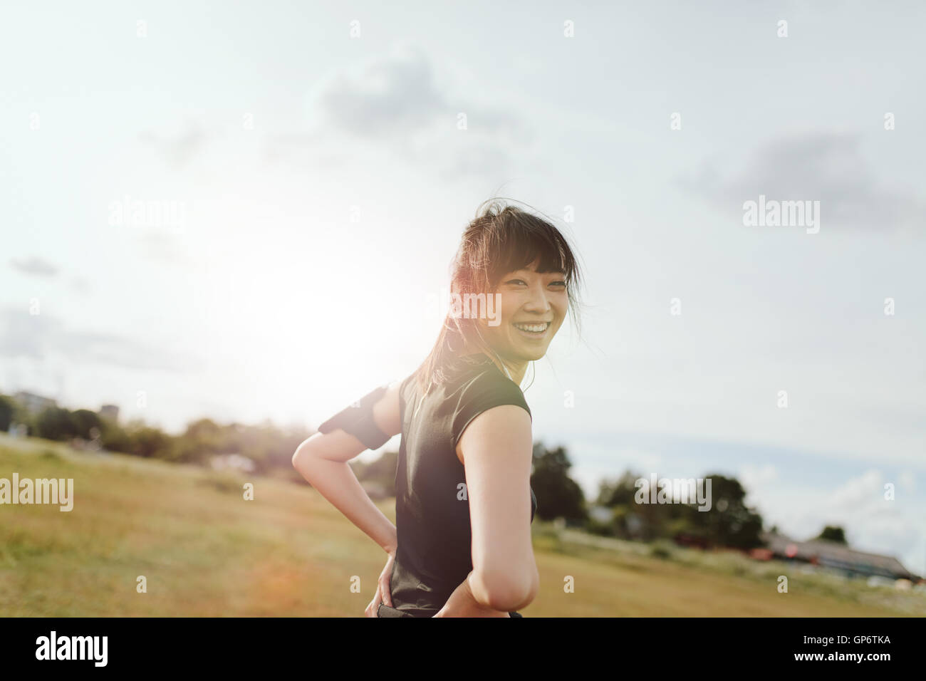 Outdoor shot of happy young woman looking at camera and smiling. fitness female on field in morning. Stock Photo