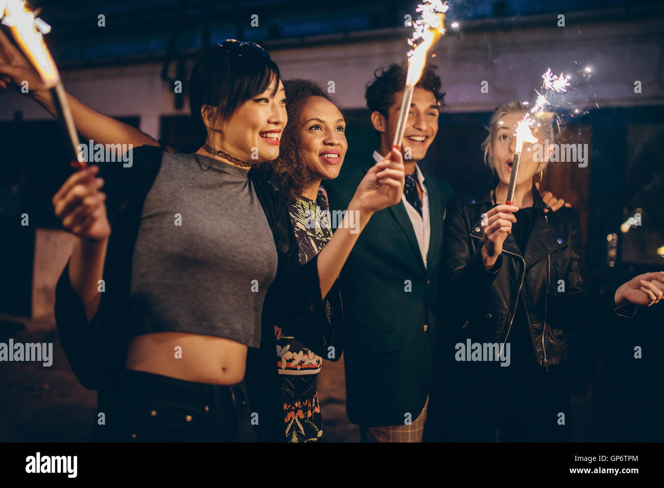 Four young friends celebrating new years eve with fireworks. Group of people enjoying with sparklers on road in evening. Stock Photo