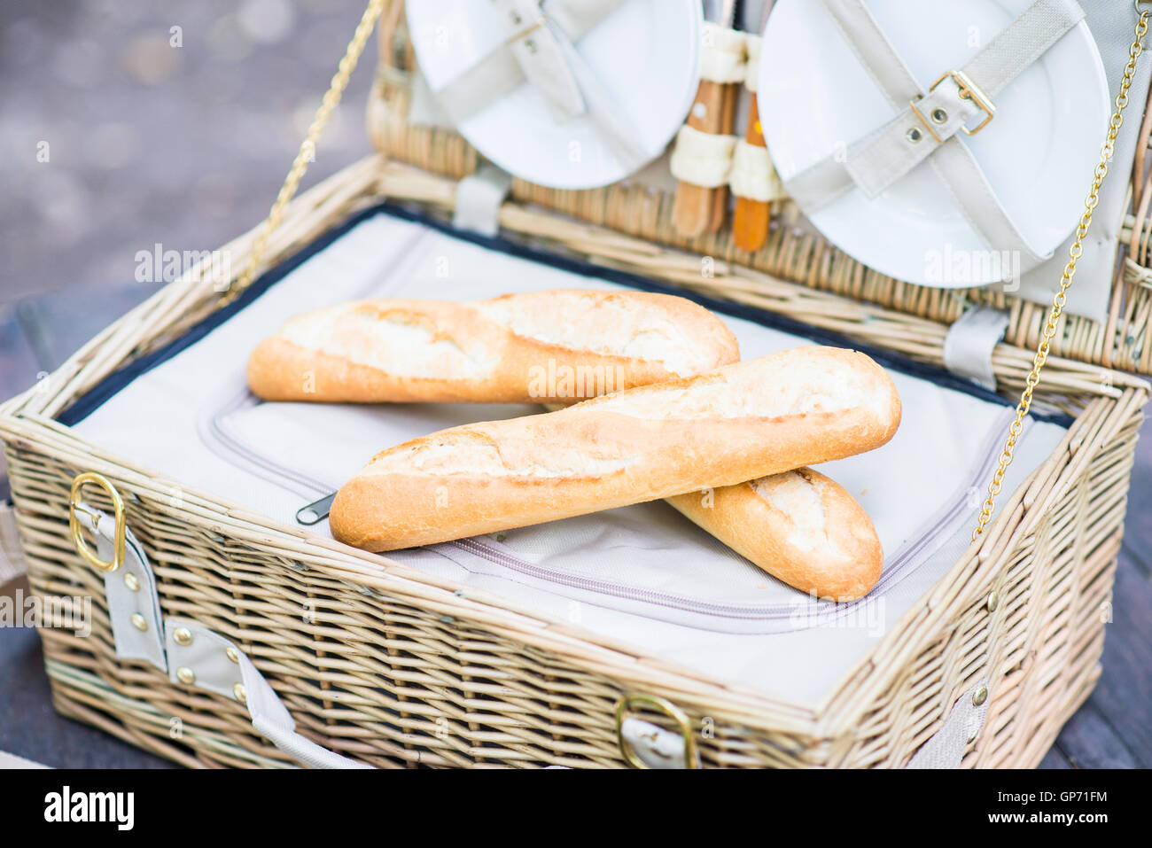 Open picnic basket with bread inside over a wooden table in the park. Stock Photo