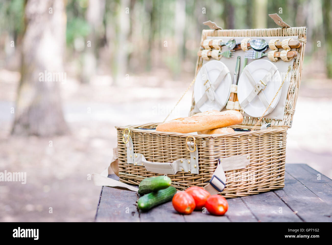 Open picnic basket with tomatoes, cucumbers and bread over a wooden table in the park. Stock Photo