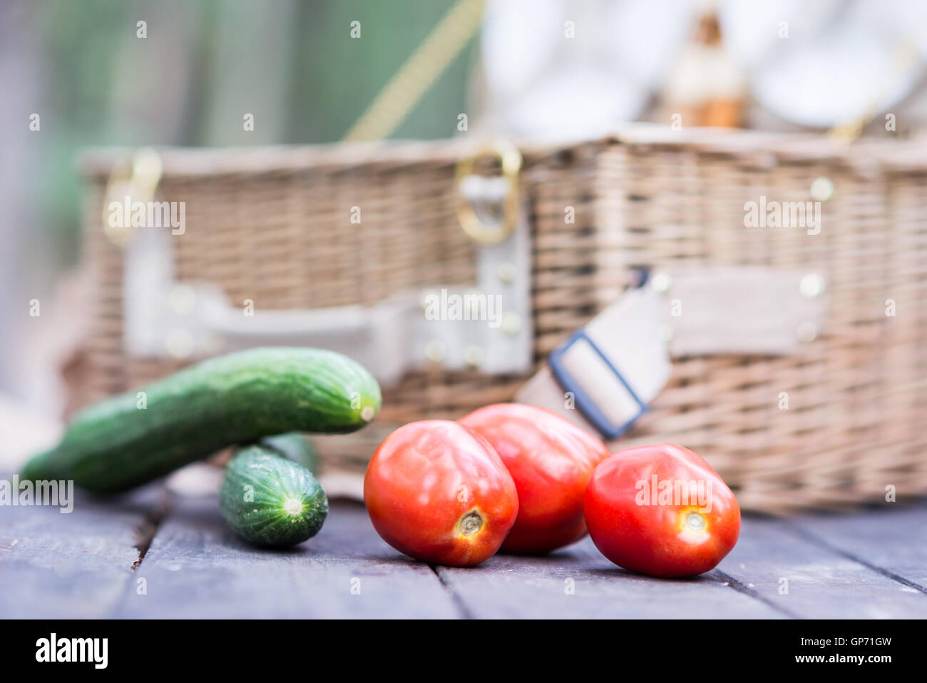 Close up of tomatoes and cucumbers over wooden table in front of an open picnic basket. Stock Photo