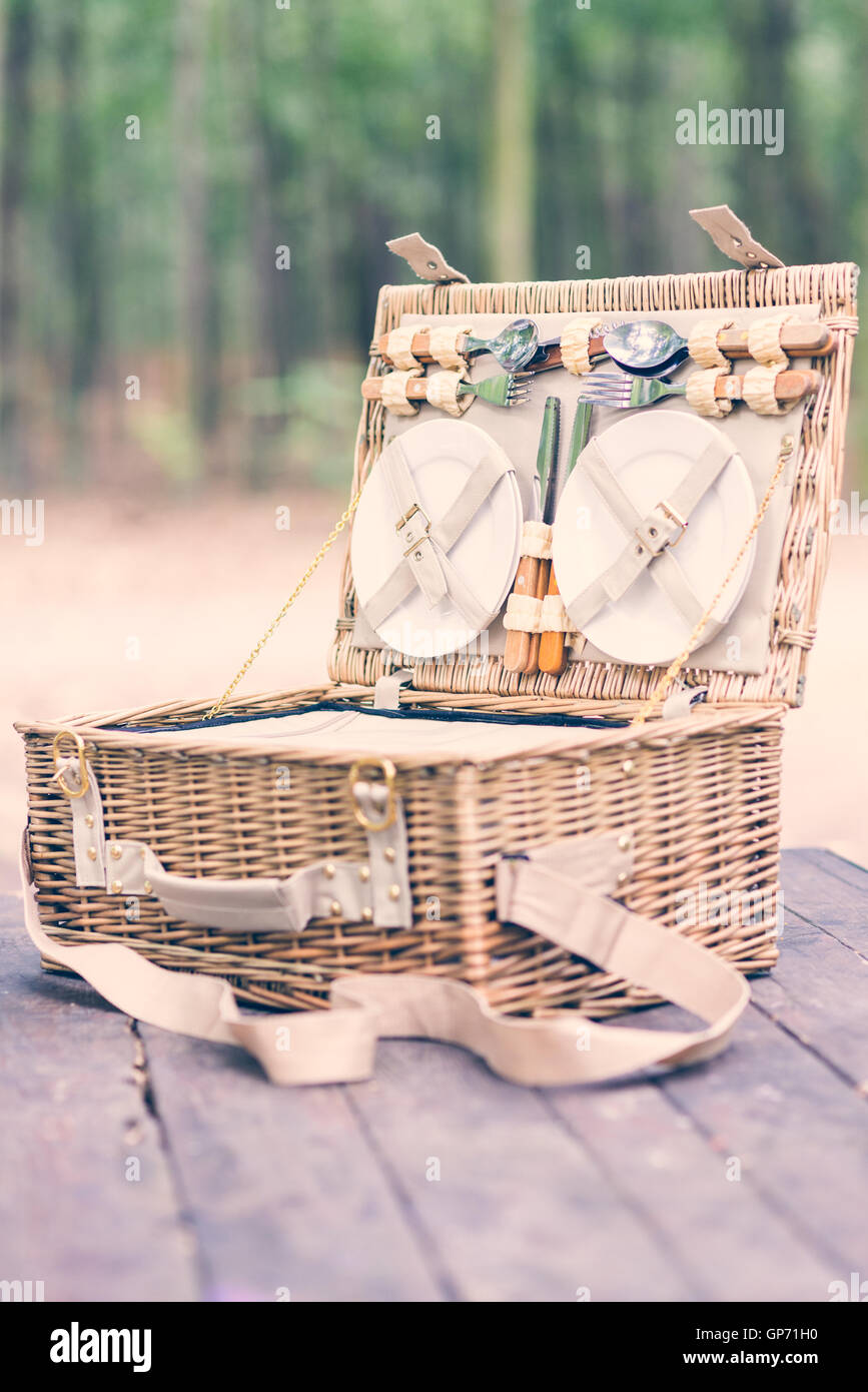 Close up of an open picnic basket over wooden table in the park. Vintage style. Stock Photo