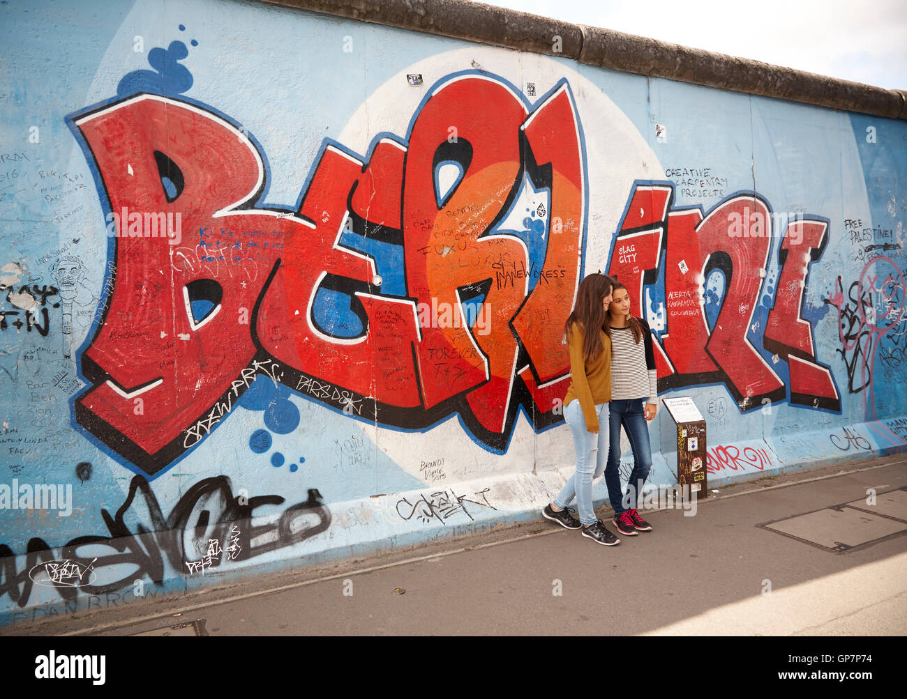 Two young ladies posing by the Berlin painting at the East Side Gallery Berlin Wall Germany. Stock Photo