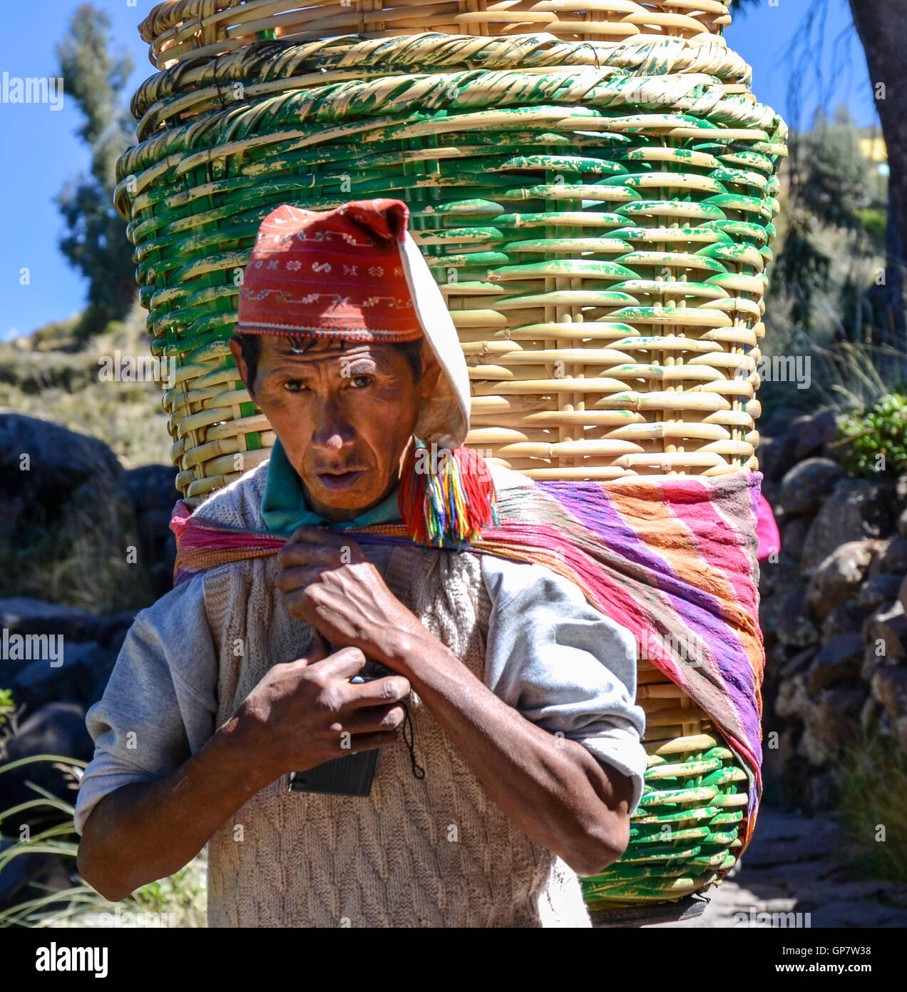 Unidentified single man in traditional clothes carrying big rattan baskets,  on the Taquile island, in Titicaca lake Stock Photo