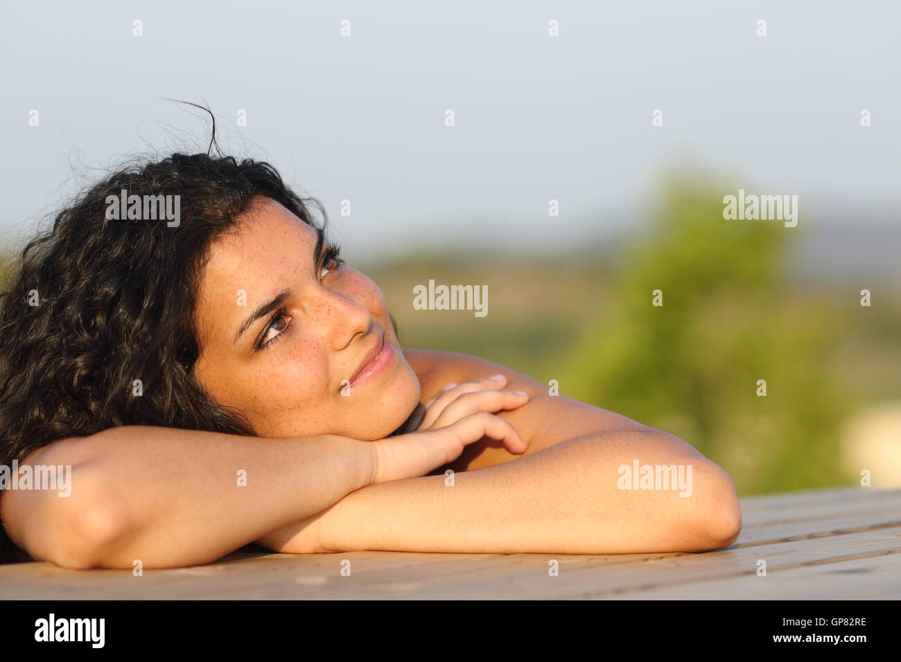 Candid girl dreaming and thinking leaning on a table outdoors Stock Photo