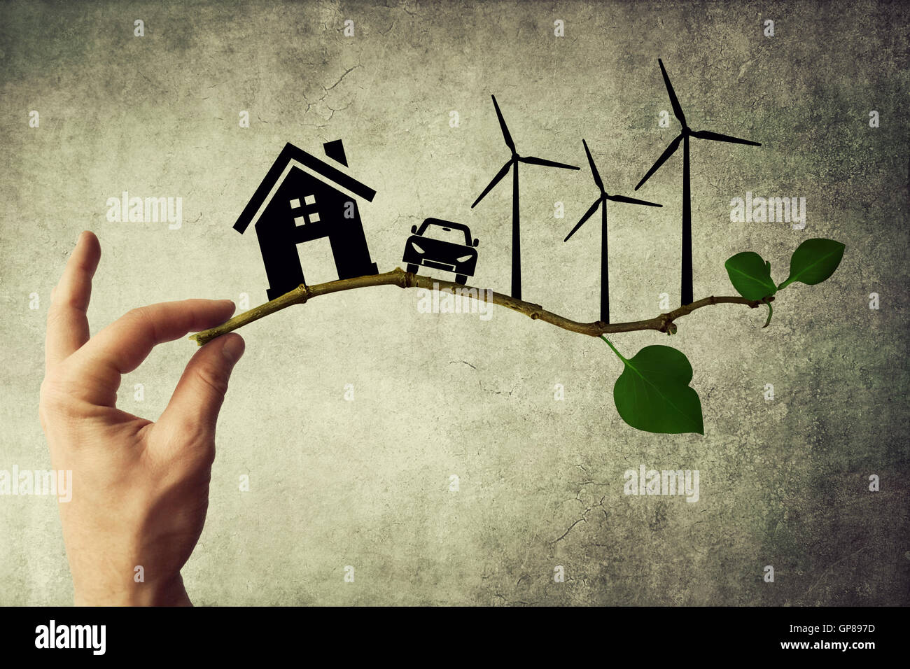 Human hand holding a tree branch. Environmental green energy concept. Silhouette of house, car and wind turbine Stock Photo