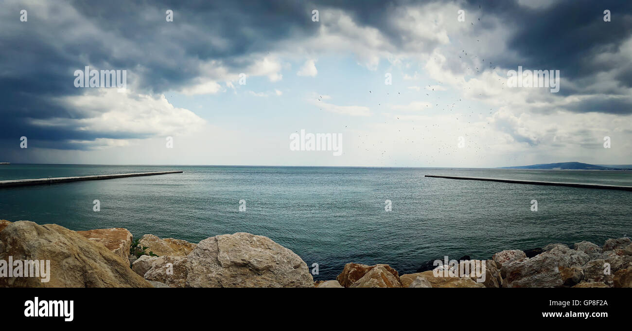 Sea landscape between two piers on the stone beach with a dramatic cloudy sky. Beautiful view at the coast of the Black Sea in B Stock Photo