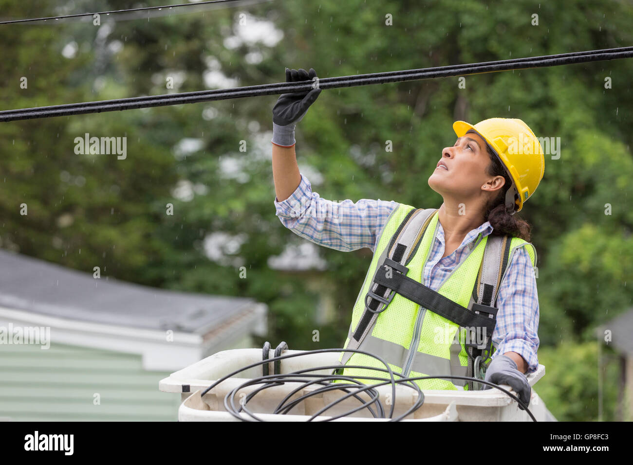 Hispanic female cable lineman examining the cables in the rain Stock