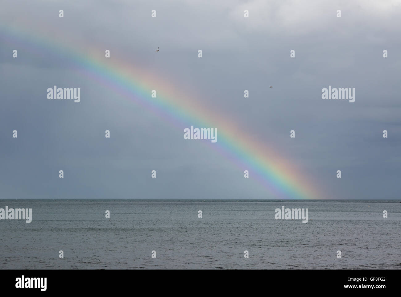 Rainbow over the sea with storm clouds Stock Photo