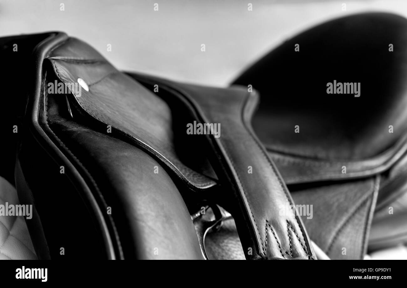 Used black dressage horse riding saddle with  white saddle pad, girth and shallow depth of field Stock Photo