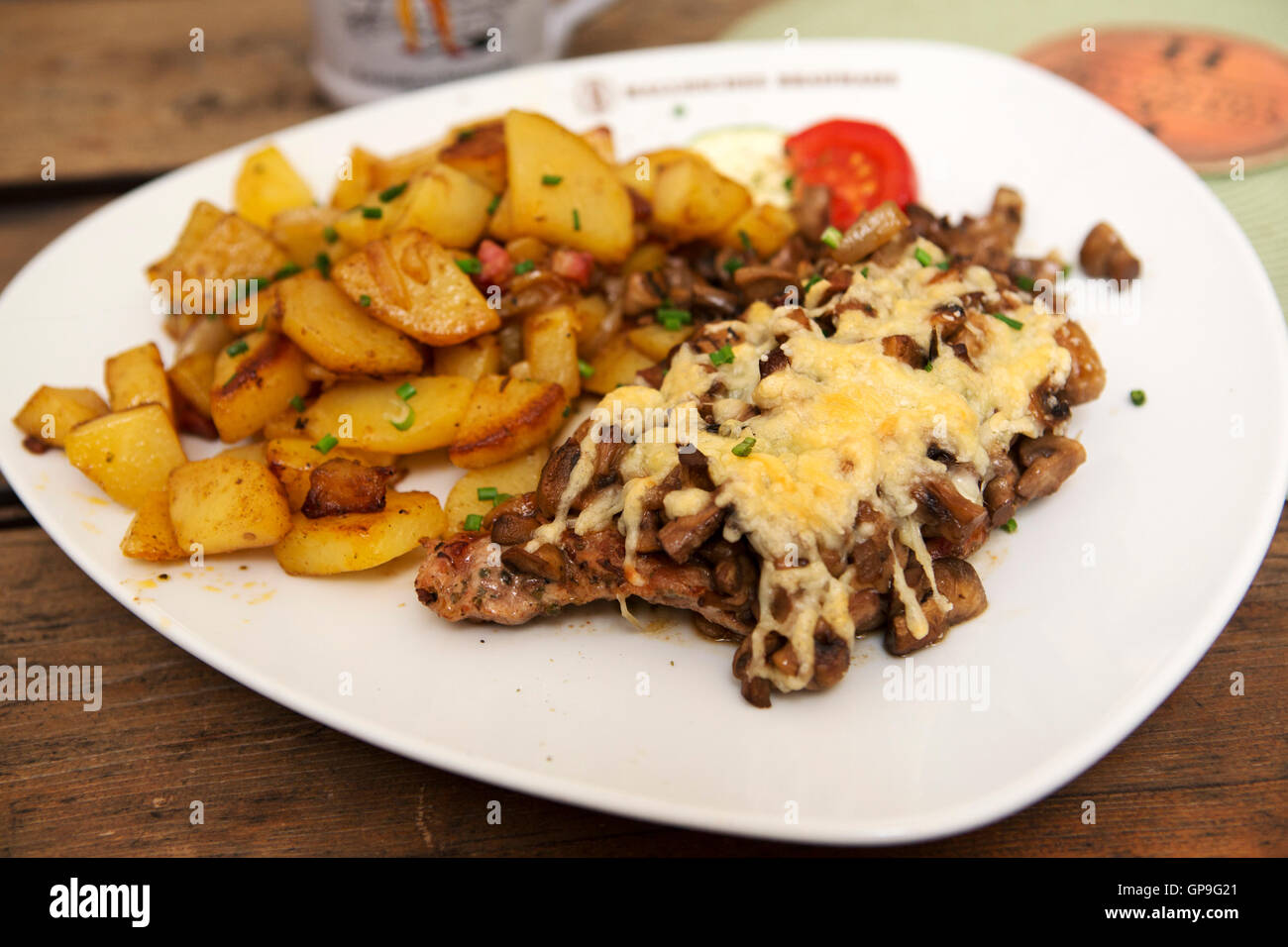 Pork steak served with cheese and mushrooms in Dresden, Germany. Bratkartoffeln (fried potatoes) are served with the dish. Stock Photo