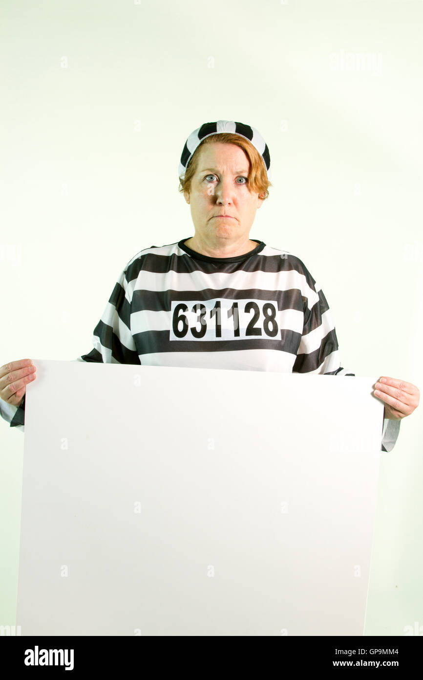 Mature woman in prison uniform holding plain white sign on white background. Stock Photo