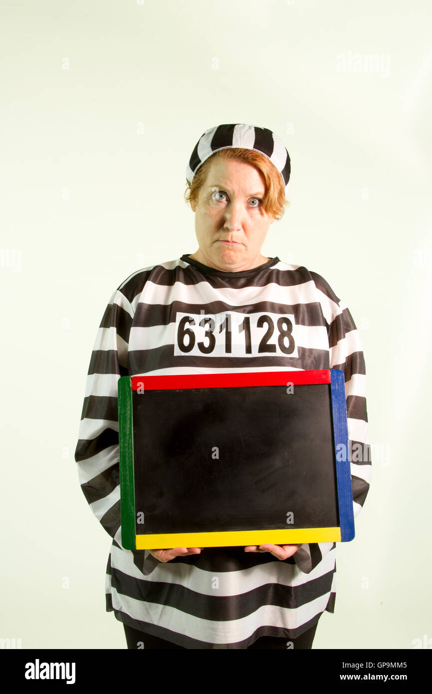 Mature woman in prison uniform holding chalkboard on white background. Stock Photo