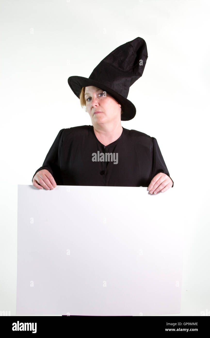 Mature woman dressed in black witch hat and robe holding blank white sign. Stock Photo
