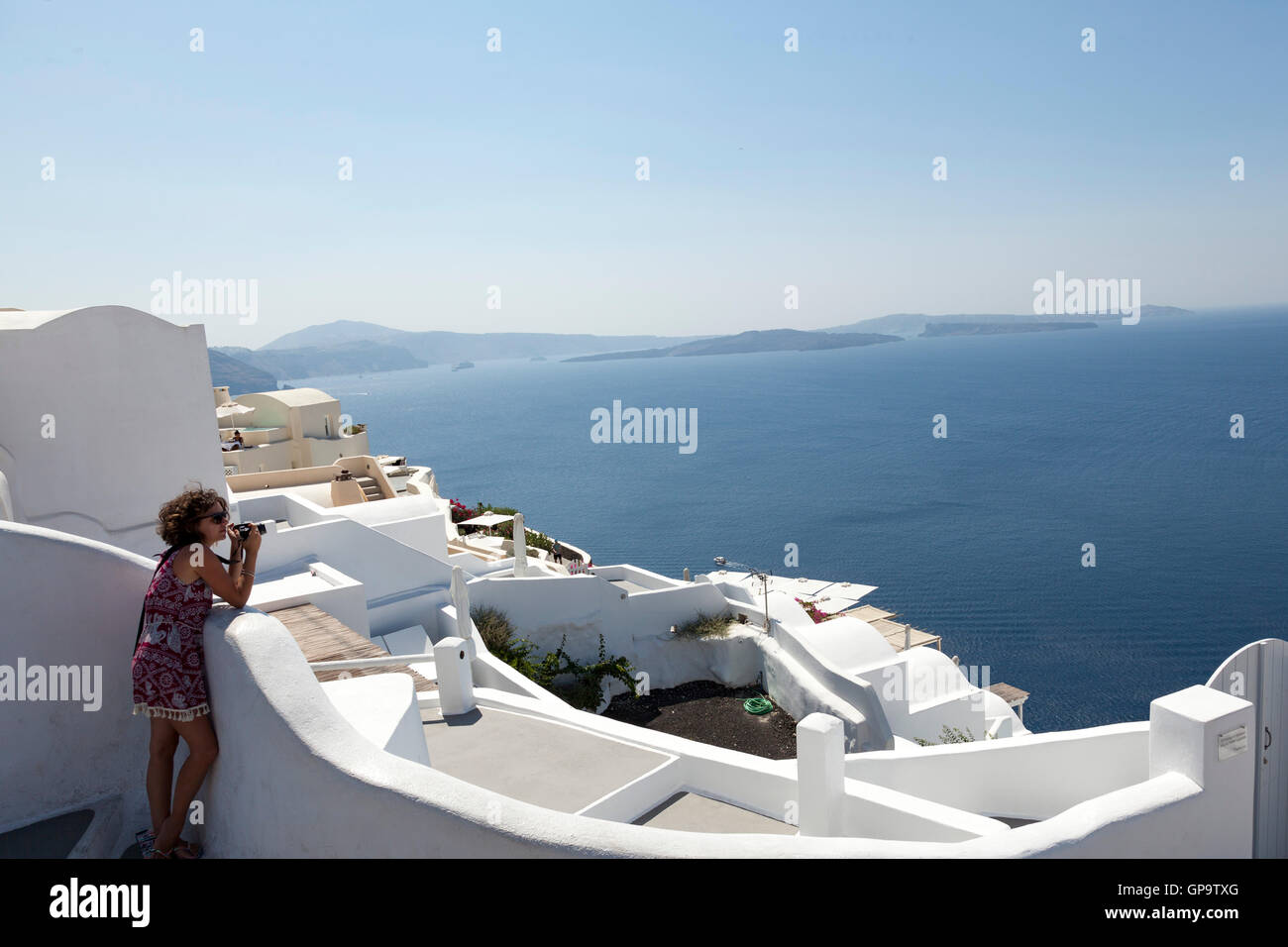 A woman takes a photograph in the town of Oia on the hot and sunny Greek island of Santorini Stock Photo