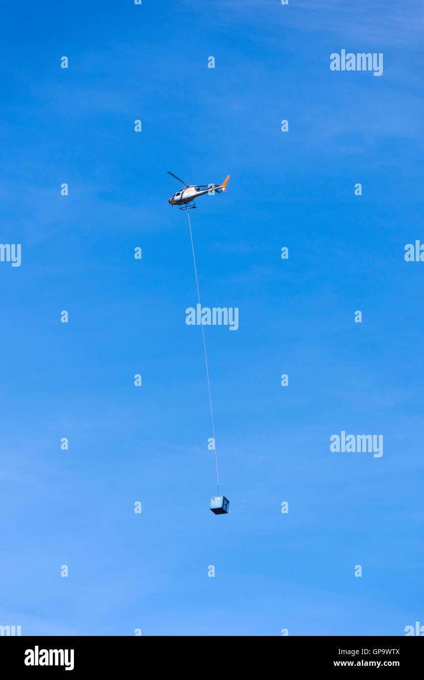 Helicopter against blue sky carrying load on the end of long cable Stock Photo