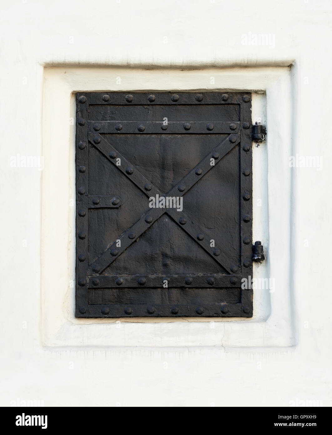 Old black metal door, closed, in white wall Stock Photo