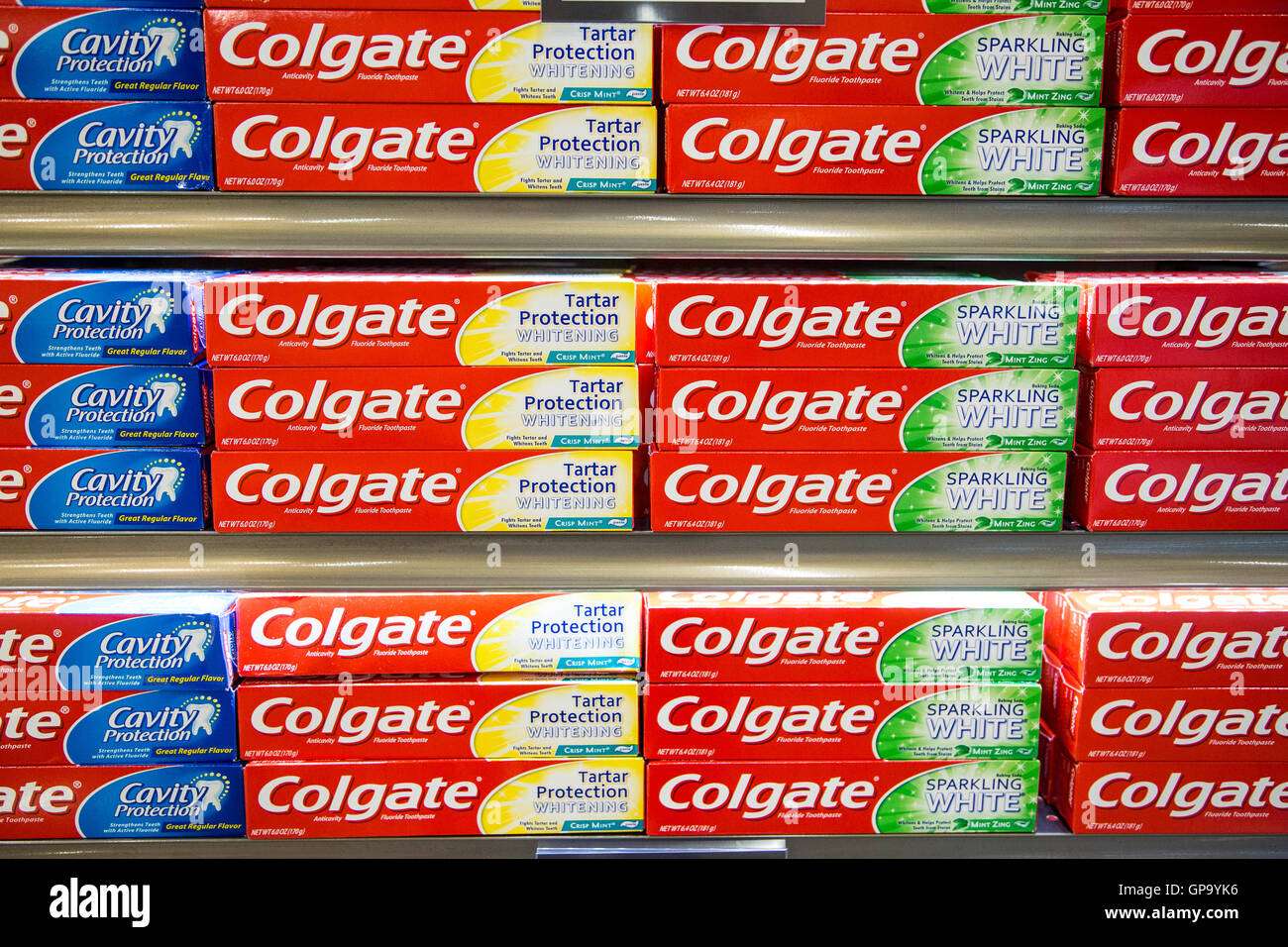 Stacks of Colgate toothpaste boxes on display on shelves at a grocery