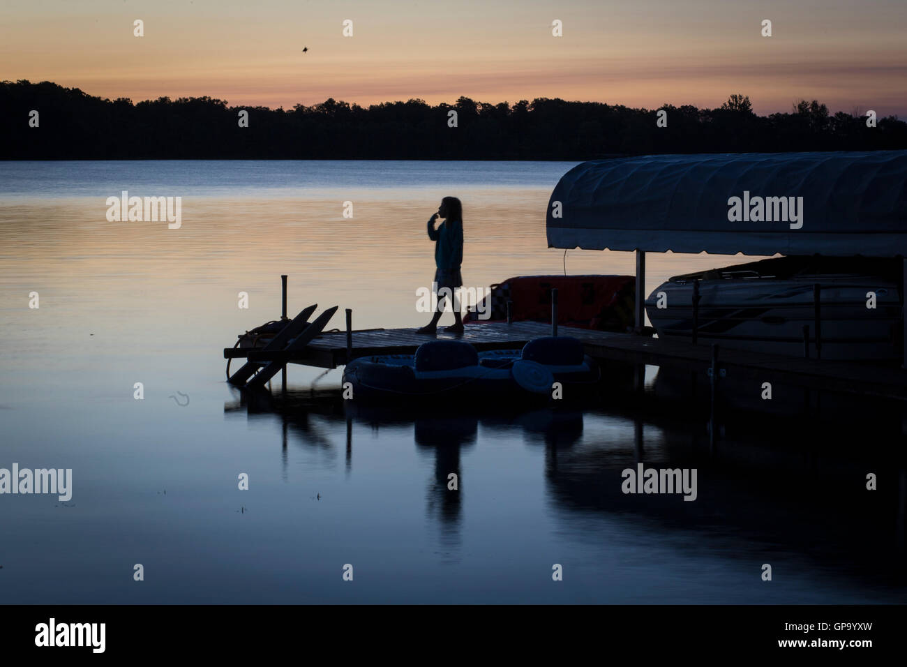 A young girl stands on a dock as the sun rises over Little Pine Lake near Aitkin, Minnesota, USA August  25, 2016 Stock Photo