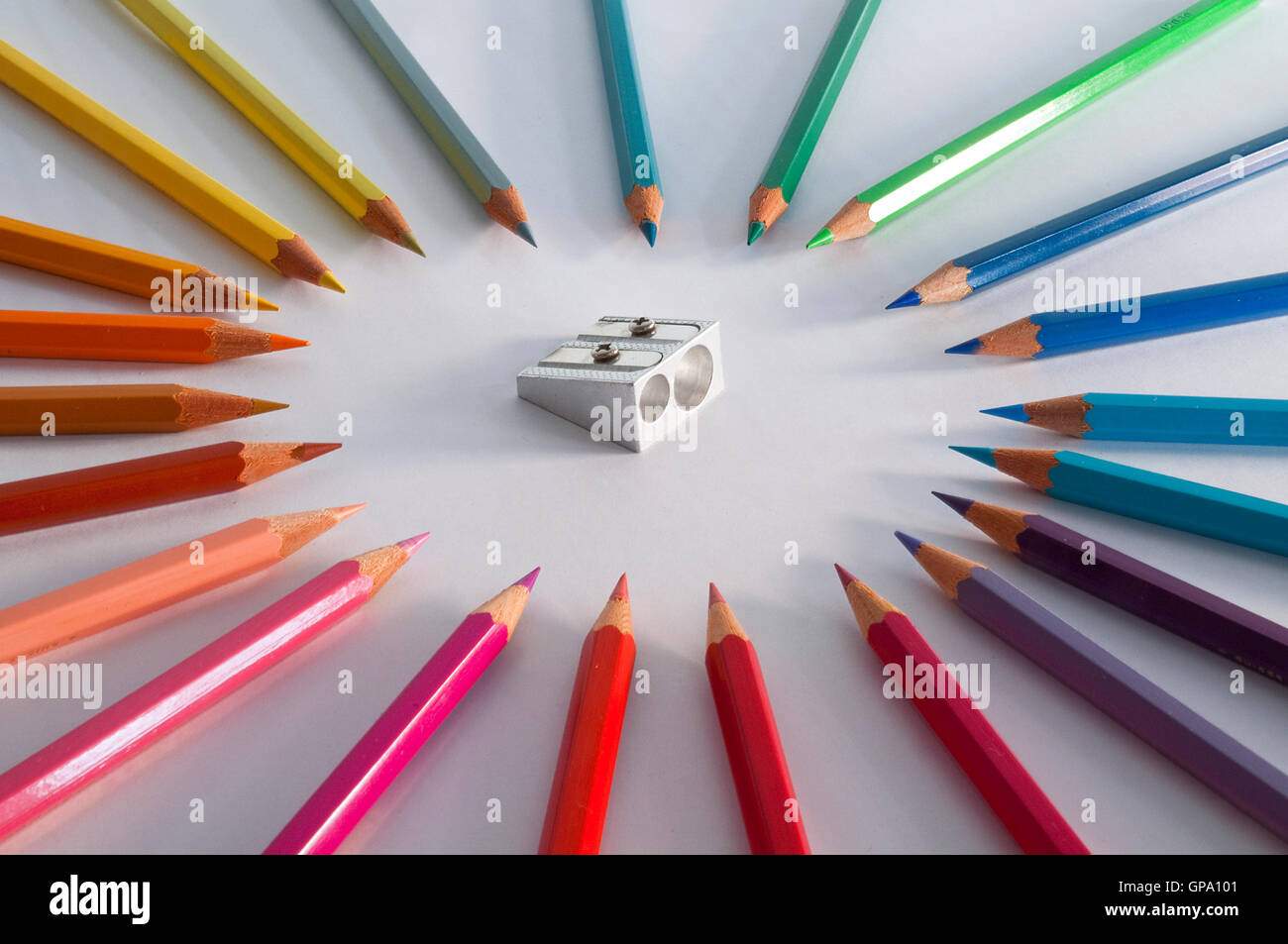 Coloured pencils surrounding menacingly a pencil sharpener. Stock Photo