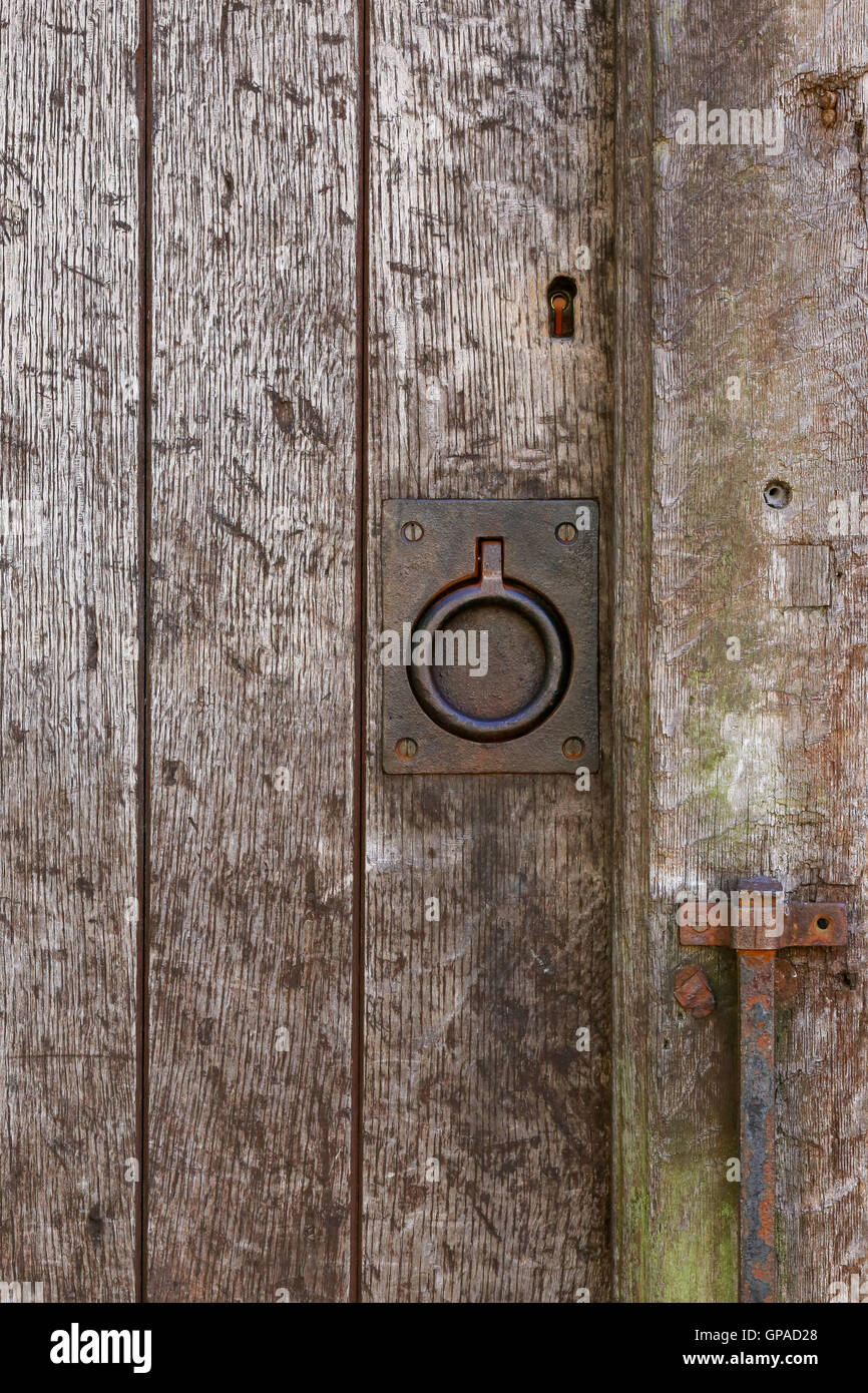 Old rusty metal ring handle on a medieval style aged timber door on stone wall background Stock Photo