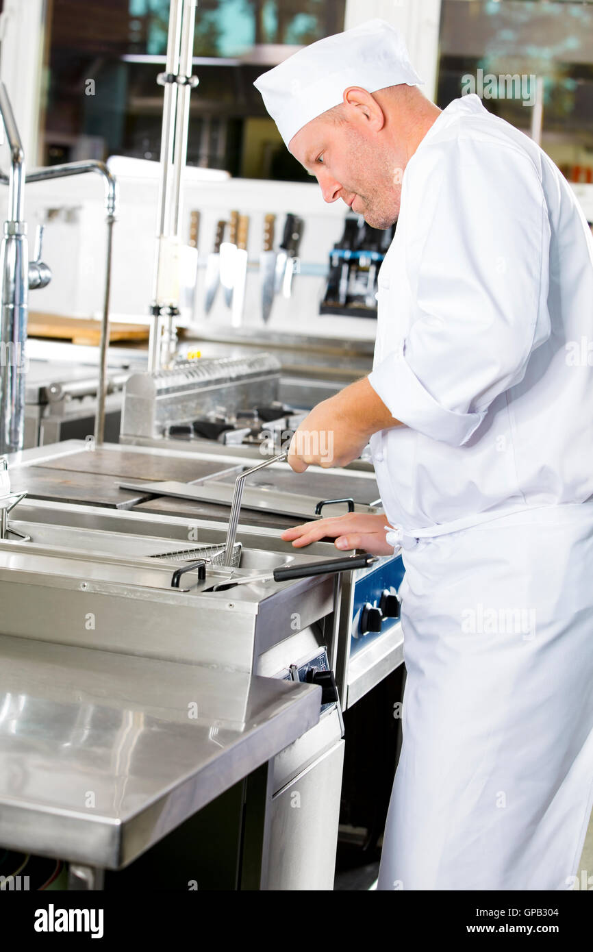 Focused chef frying food in fryer at large industrial kitchen Stock Photo