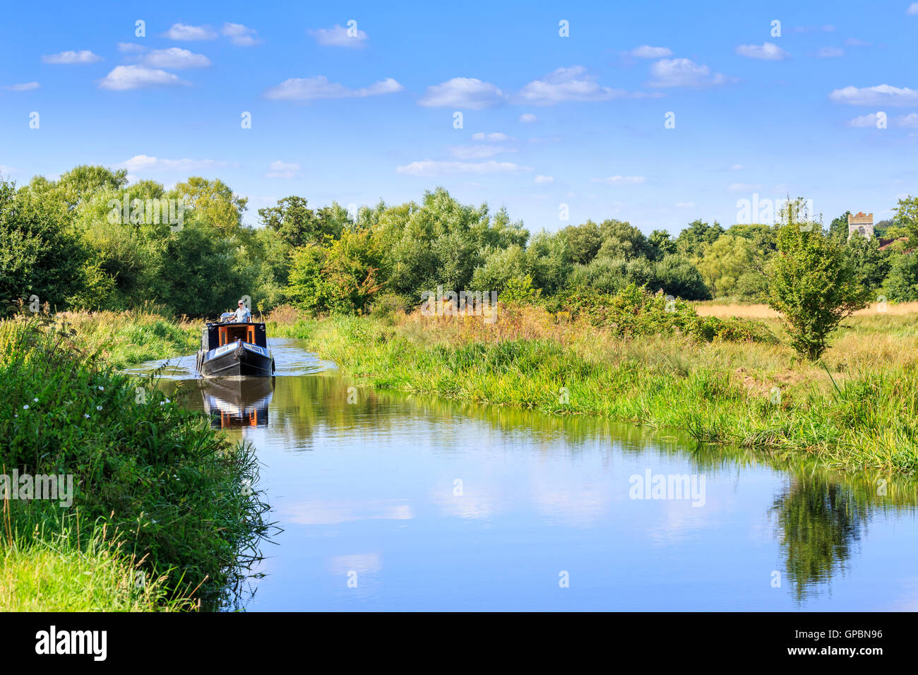 Narrowboat leisurely cruising on the Wey Navigation near Send, Surrey on a calm sunny day with blue sky in summer - peaceful staycation lifestyle Stock Photo