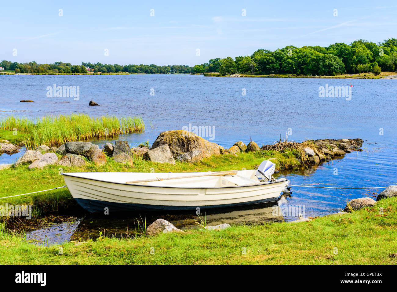 Small open rowboat moored in an old, narrow dug out bay beside a small stone boulder pier so typical for the south Swedish coast Stock Photo