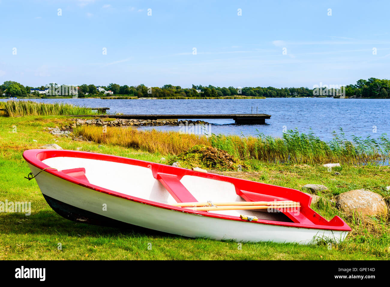 Small red and white rowboat dragged up on land with the coastline in the background.  Skavkulla in Karlskrona archipelago, Swede Stock Photo
