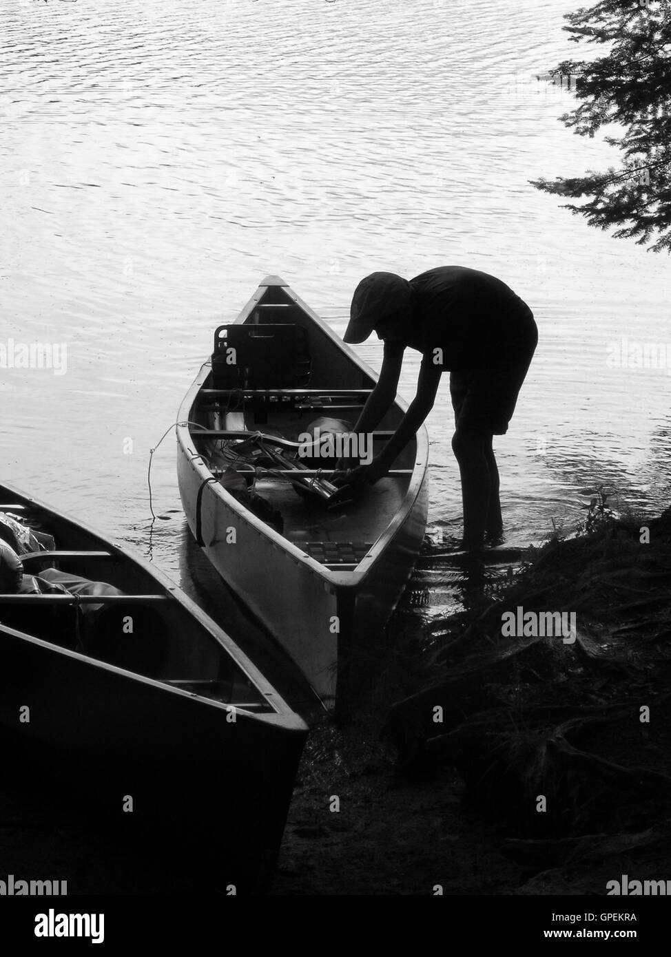 Boy Loading Canoe in Silhouette on Lake Stock Photo