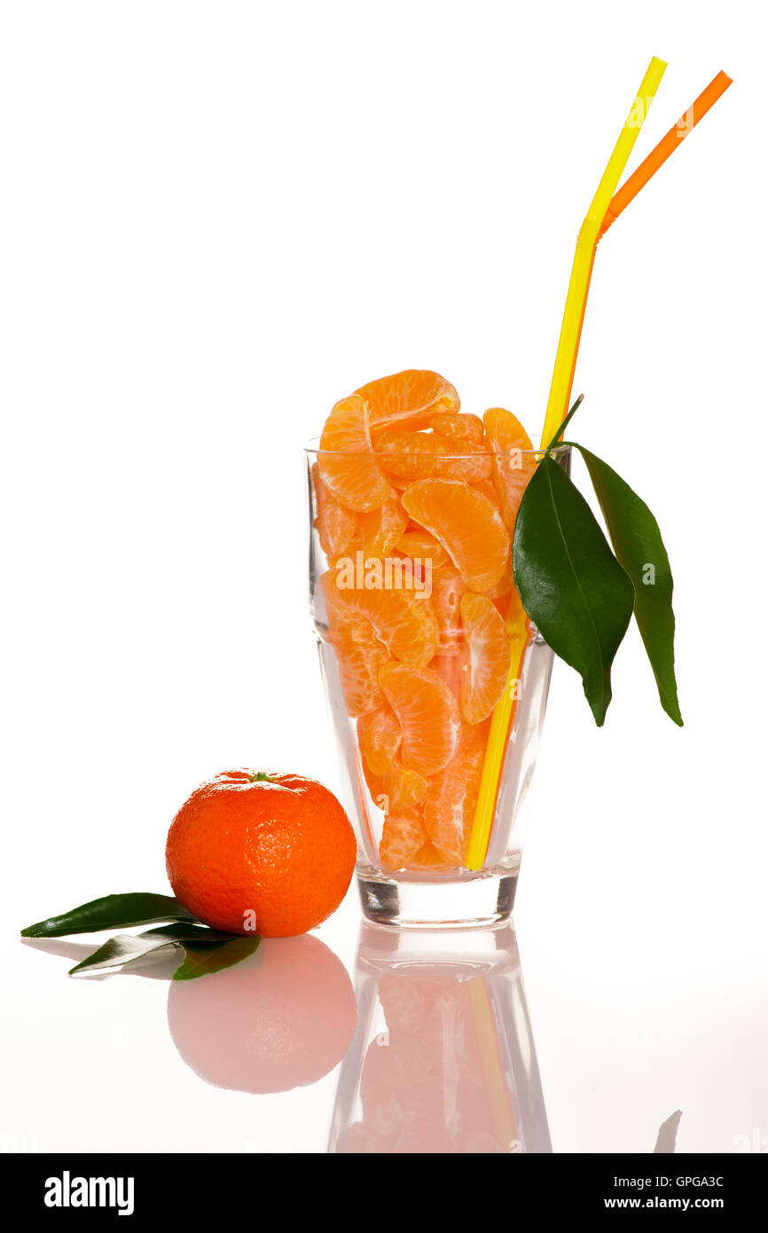 Big glass filled with orange mandarin citrus fruit slices, decorated with straw and green leafs representing fresh natural juice Stock Photo