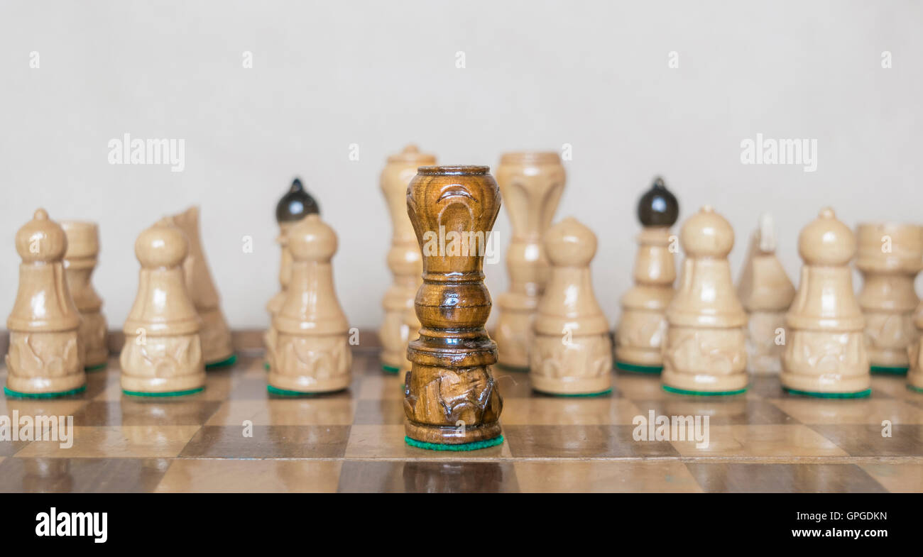 Black queen in front of white figures on chess table. Stock Photo