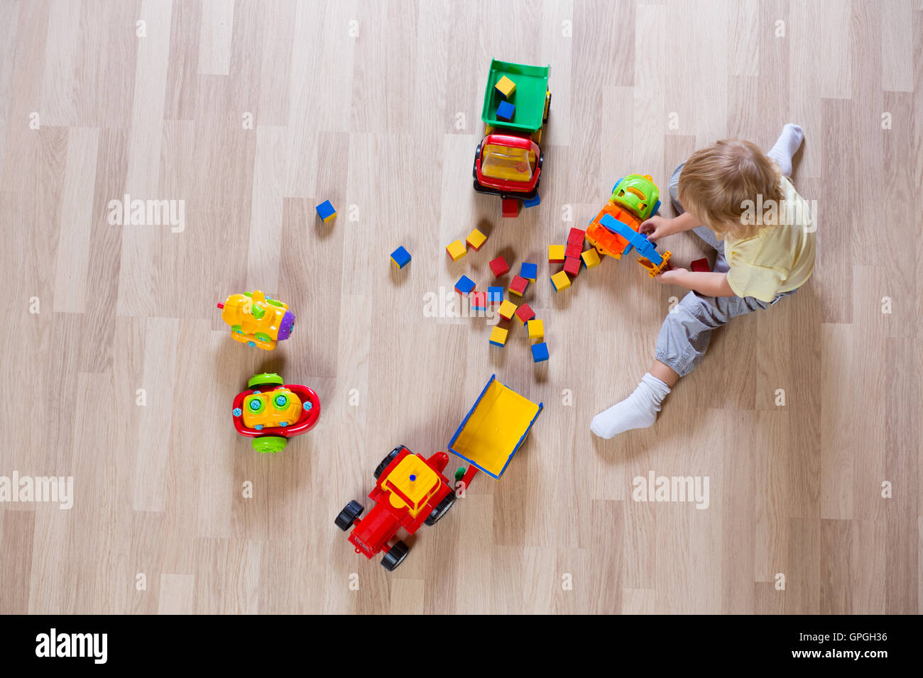 Little blond kid boy playing with colorful car toys on floor top view Stock Photo