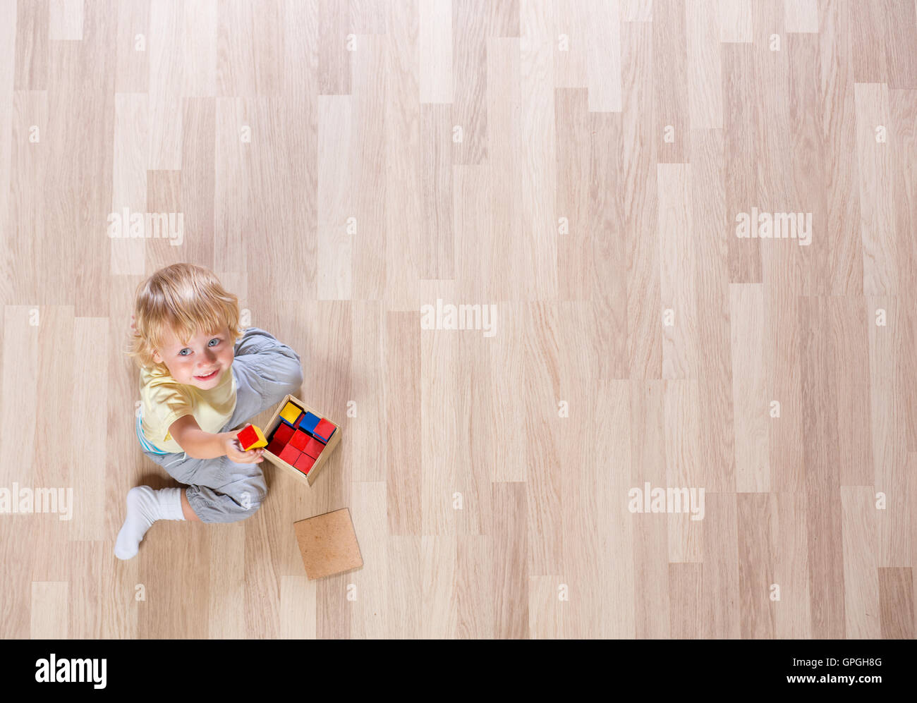Little blond kid boy playing with colorful building blocks on floor top view Stock Photo