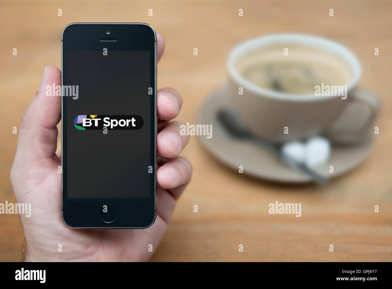A man looks at his iPhone which displays the BT Sport television station logo, with a cup of coffee (Editorial use only). Stock Photo