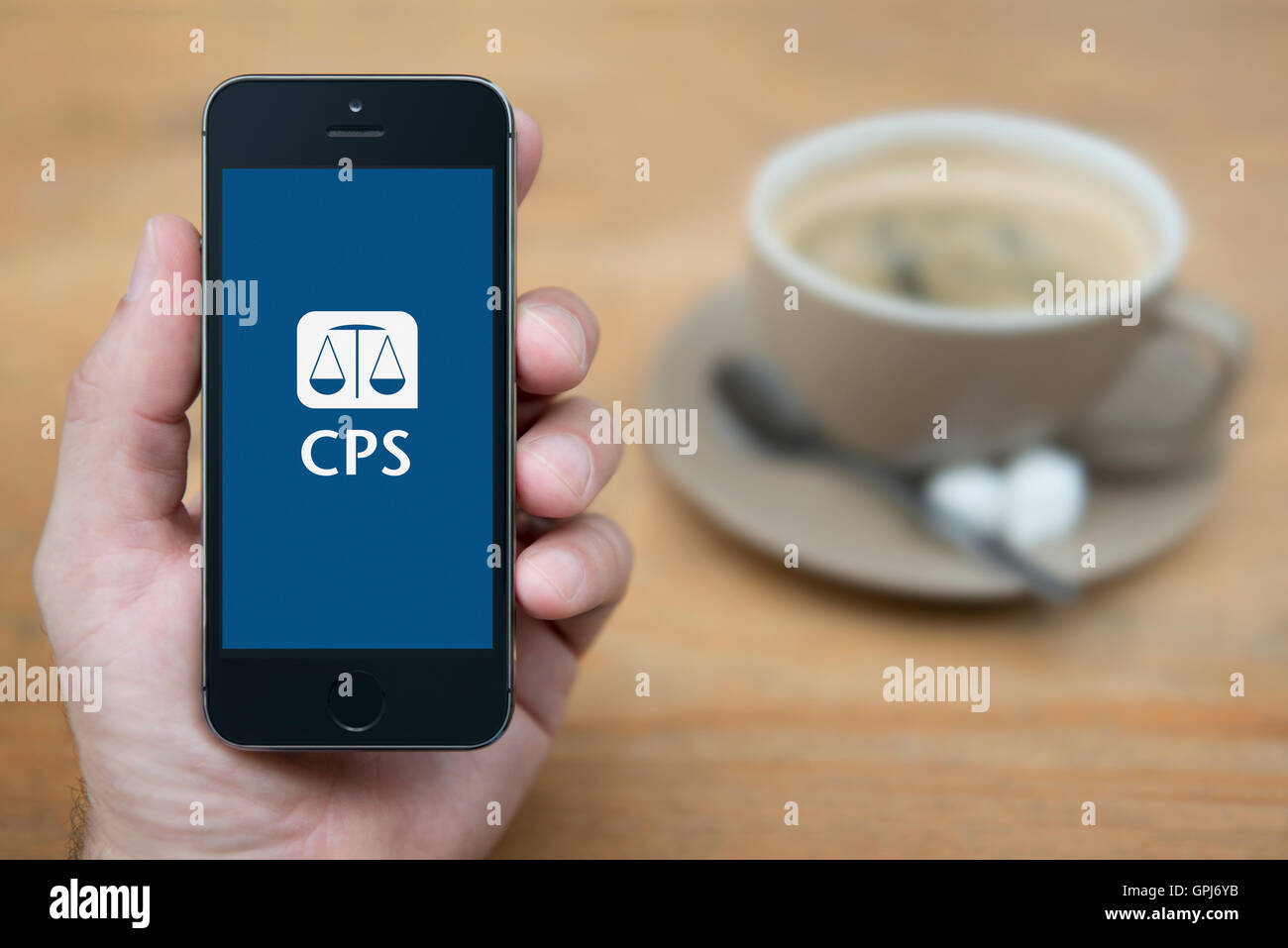 A man looks at his iPhone which displays the UK Government Crown Prosecution Service logo, with coffee (Editorial use only). Stock Photo
