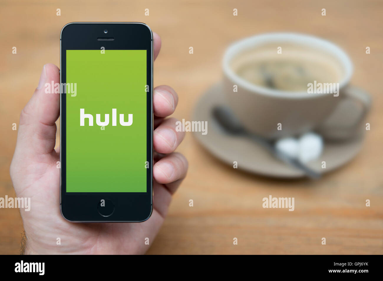 A man looks at his iPhone which displays the Hulu video subscription logo, while sat with a cup of coffee (Editorial use only). Stock Photo