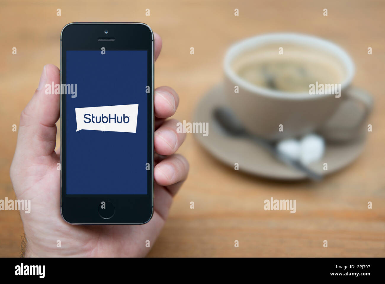 A man looks at his iPhone which displays the StubHub logo, while sat with a cup of coffee (Editorial use only). Stock Photo