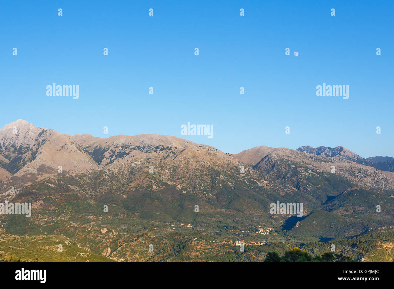 The emblematic Taygetus Mountain with the moon rising over its peaks early in the afternoon in Messenia, Greece Stock Photo