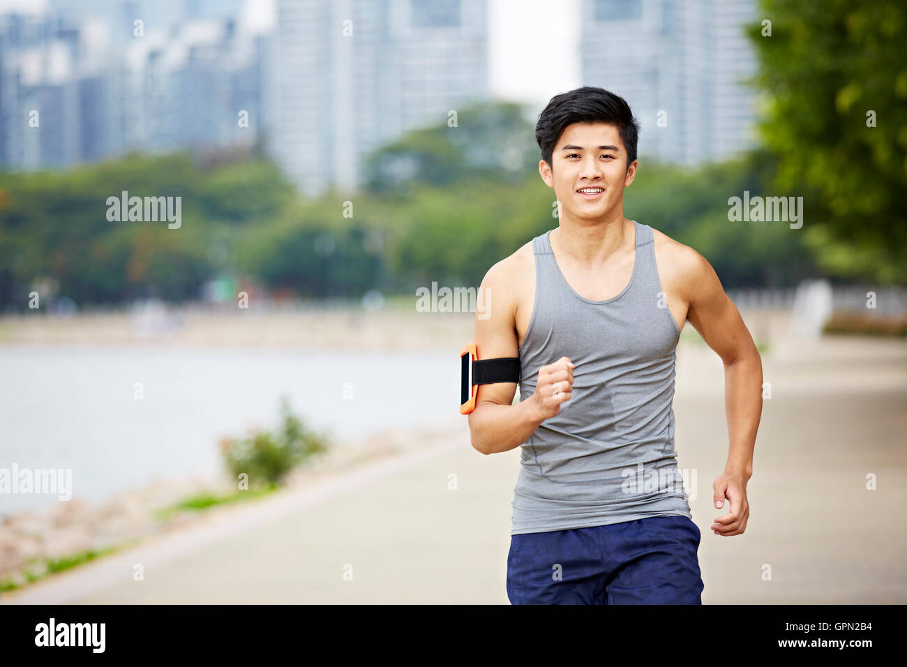 young handsome asian jogger running exercising in city park wearing fitness tracker Stock Photo