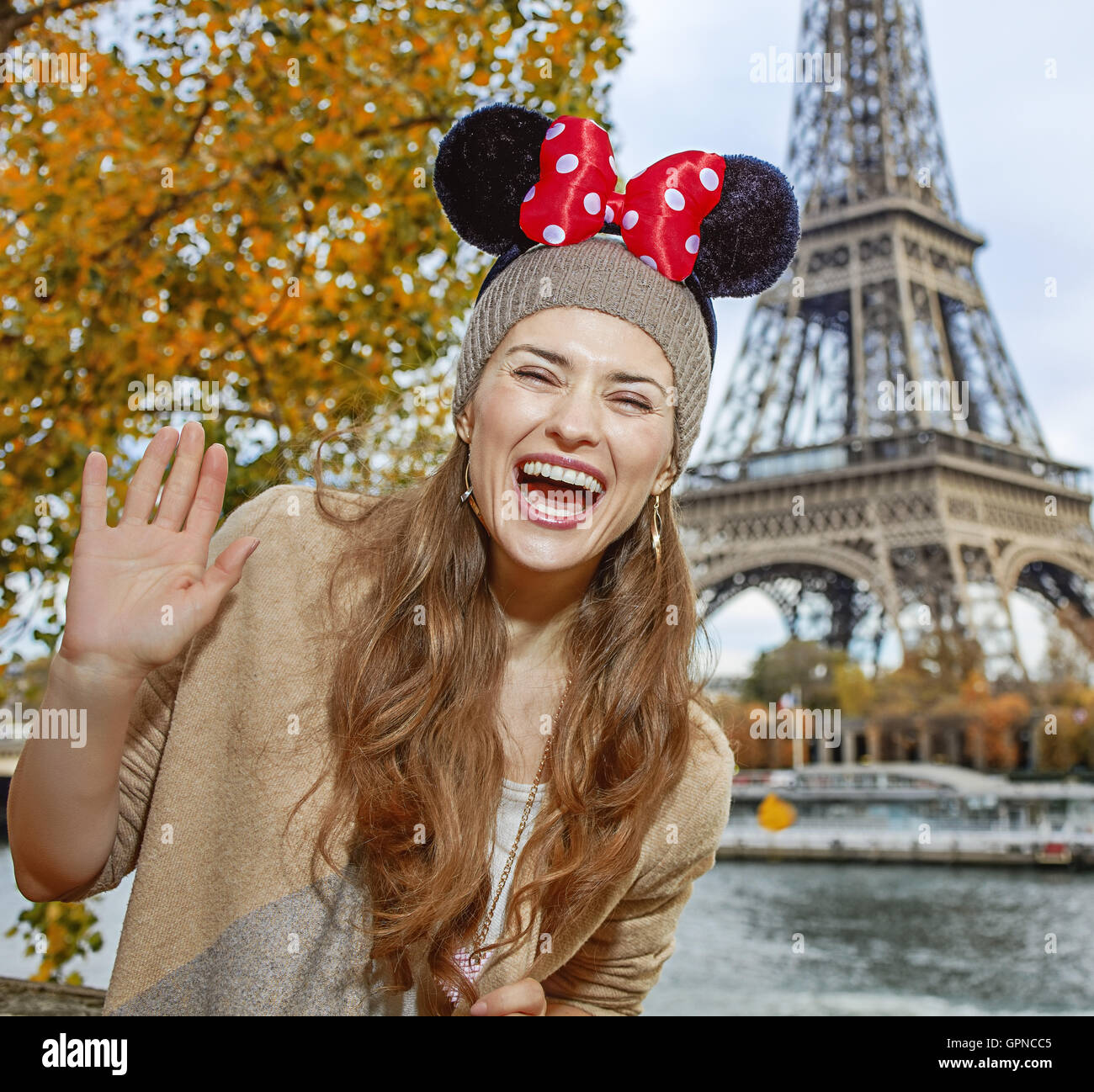 Perfect autumn holidays in Disneyland and Paris. Portrait of happy tourist woman wearing Minnie Mouse Ears handwaving on embankm Stock Photo