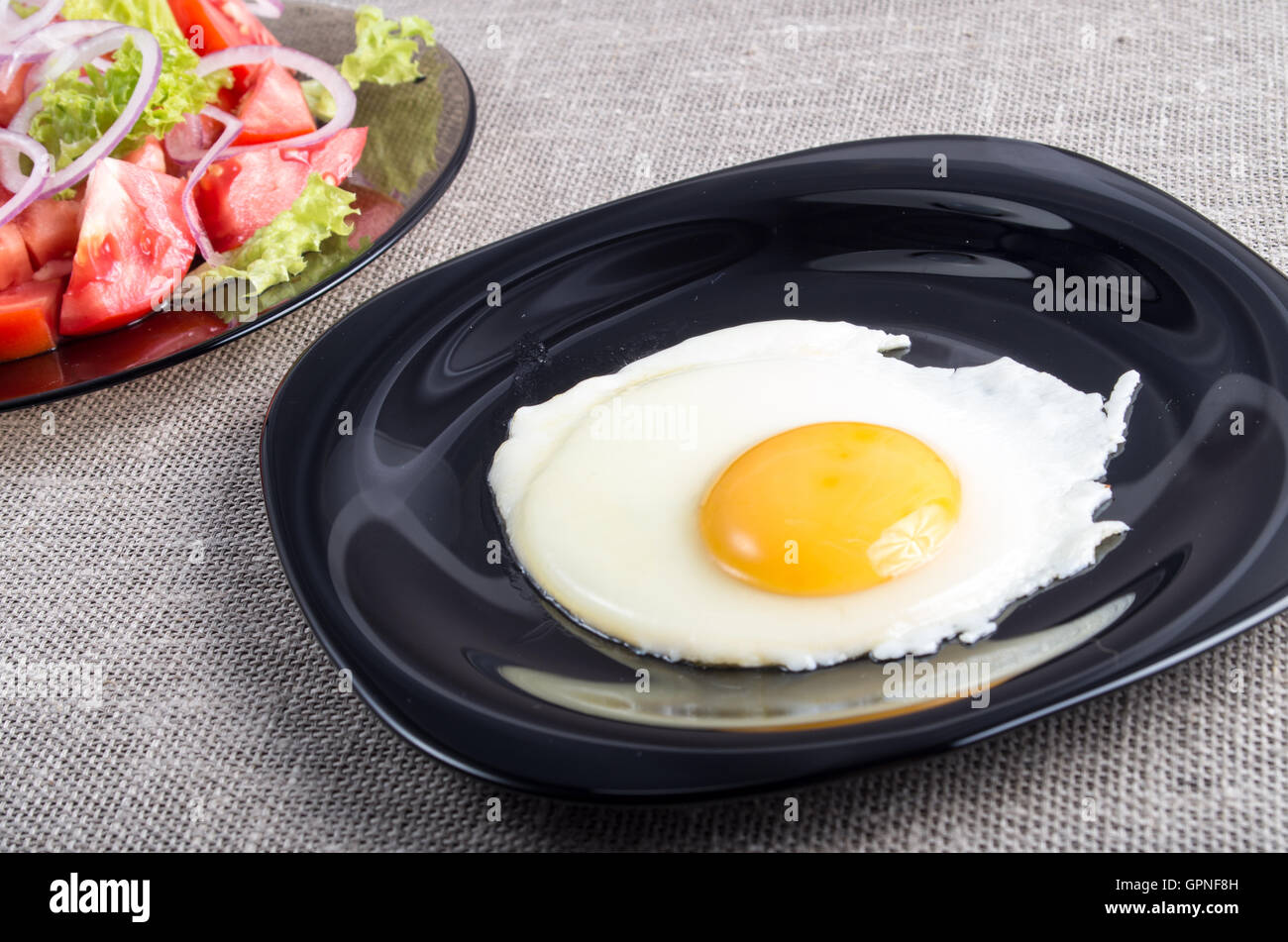 Useful homemade breakfast of fried egg and a salad of chopped tomato on a plate on tabletop Stock Photo