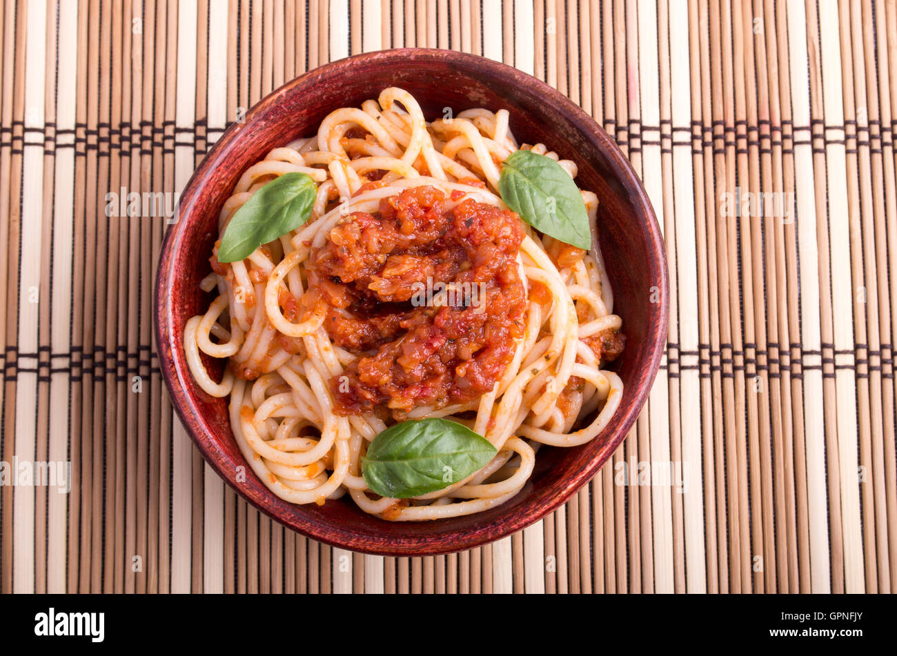 Top view of a thin spaghetti with tomato relish and basil leaves in a
