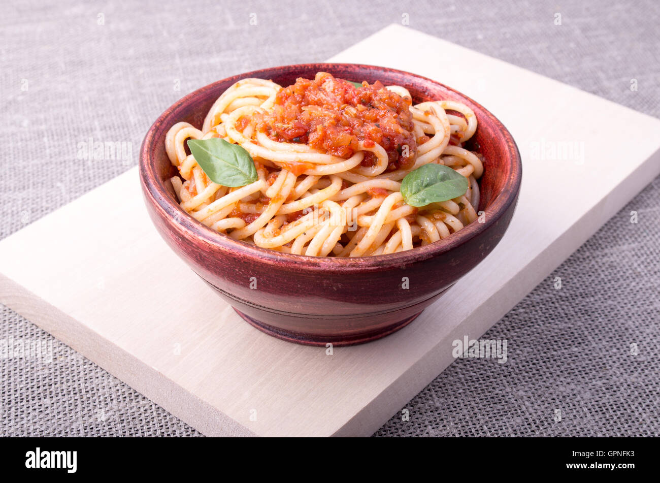 Cooked spaghetti with tomato relish and basil leaves in a brown small