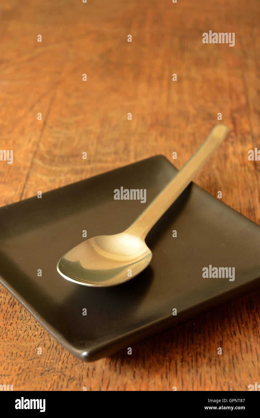 Silver spoon lying on black square plate. Stock Photo