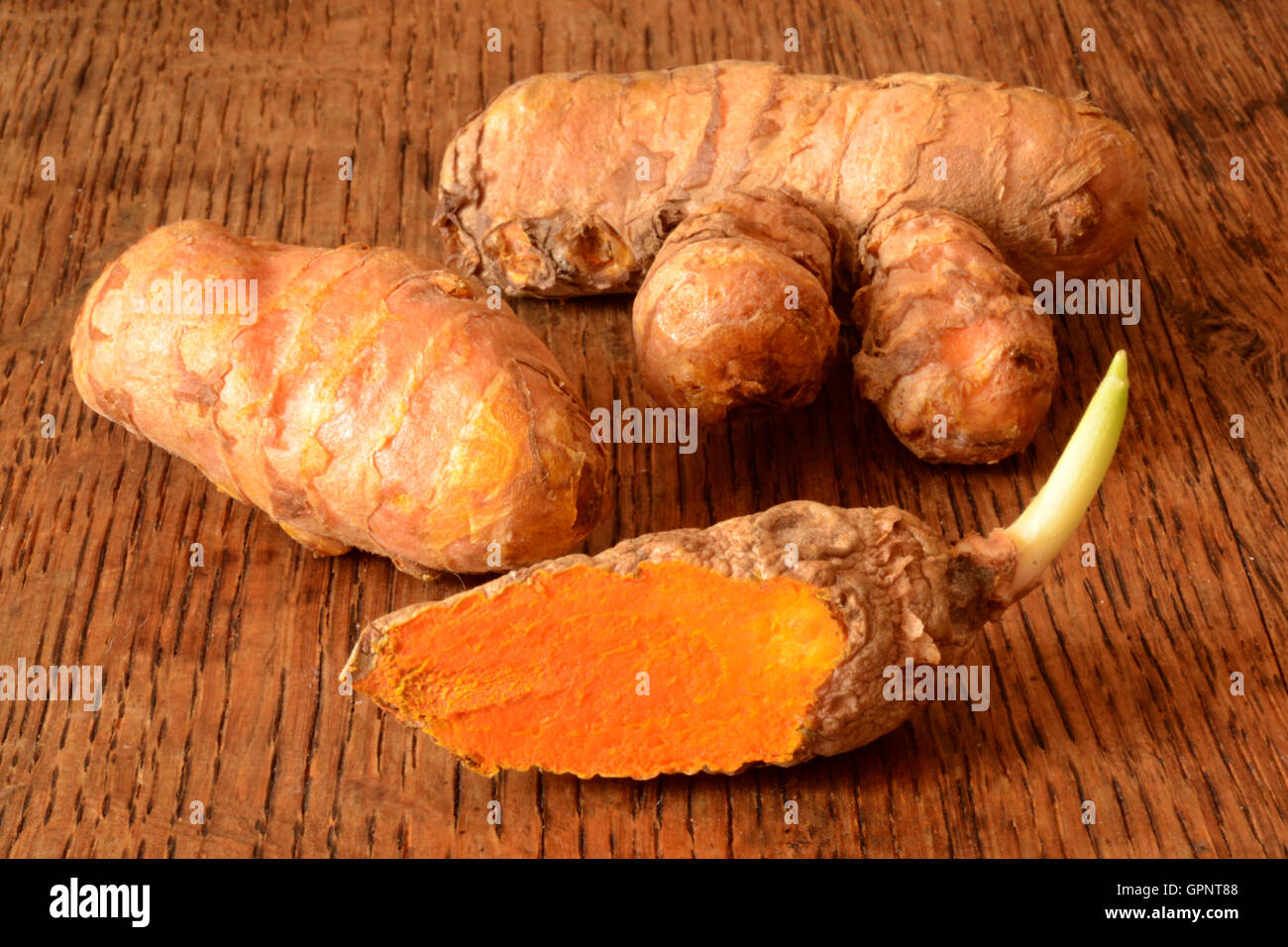 Turmeric root lying on dark wood table. one of the roots is sliced and has begun to sprout