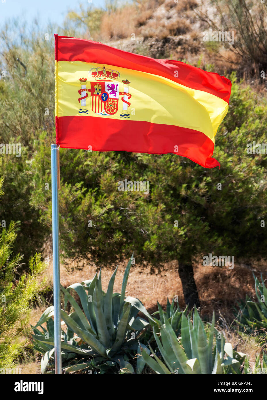 Spanish flag on a pole flying against authentic Spanish countryside, focus on flag.  shot outdoors in  inland Granada, Stock Photo